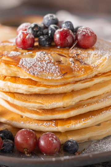 Fluffy sourdough discard pancakes stacked on a plate with fruit and syrup, golden brown and light in texture