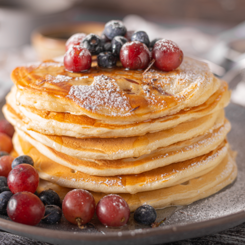 Fluffy sourdough discard pancakes stacked on a plate with fruit and syrup, golden brown and light in texture