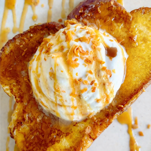 Toasted coconut French toast topped with whipped cream and caramel drizzle on a white plate.