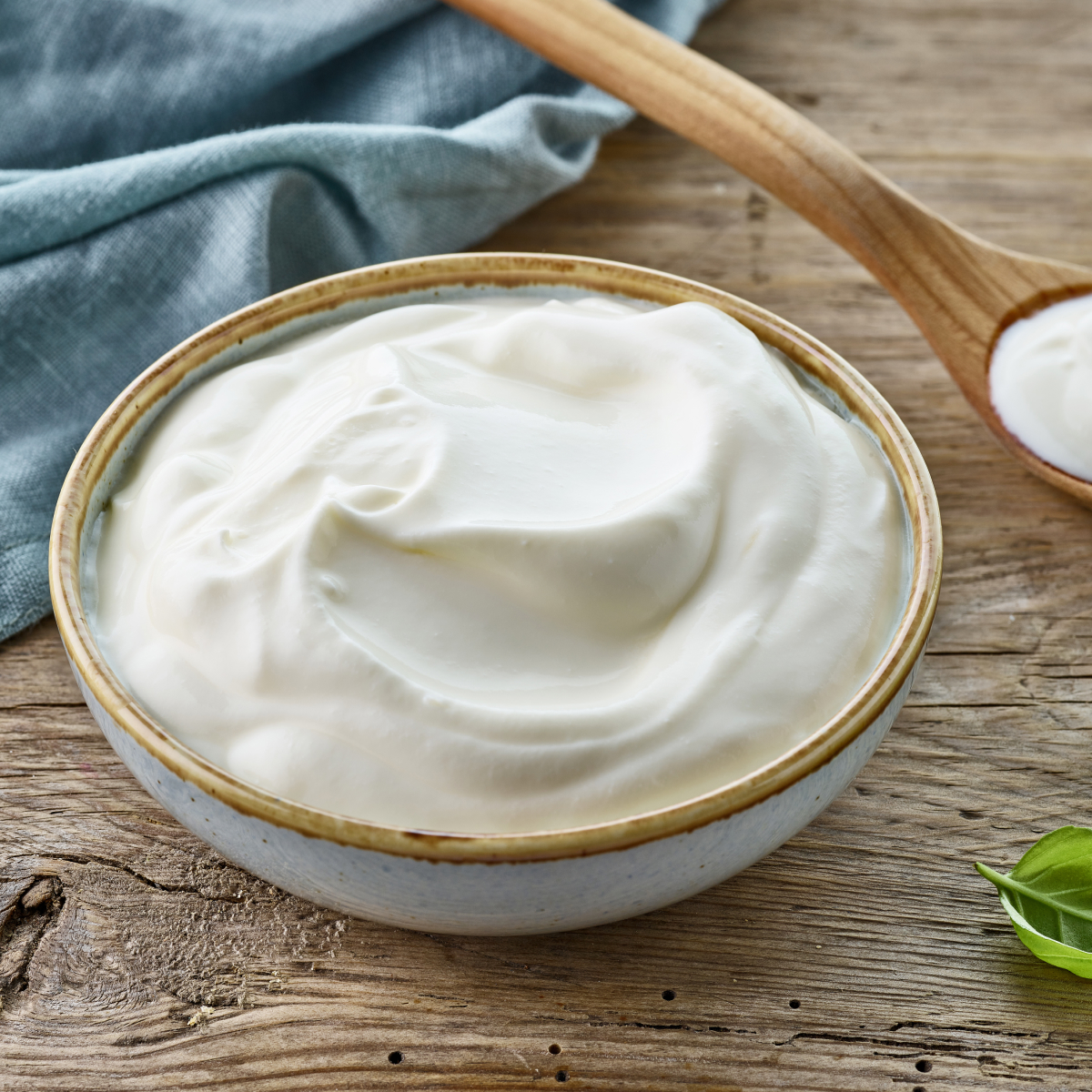 A ceramic bowl filled with thick sour cream on a wooden surface, showing its smooth and creamy texture.