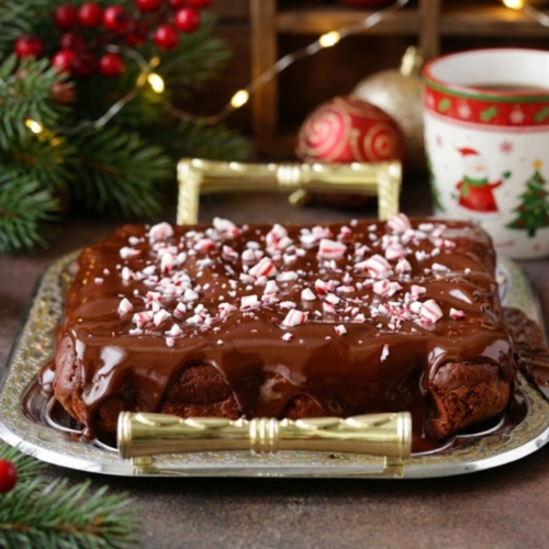 Fudgy peppermint hot chocolate brownies topped with silky chocolate ganache and crushed candy canes on a holiday baking tray.