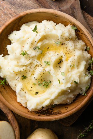 Large serving bowl of creamy mashed potatoes topped with butter and herbs, ready for a holiday meal.