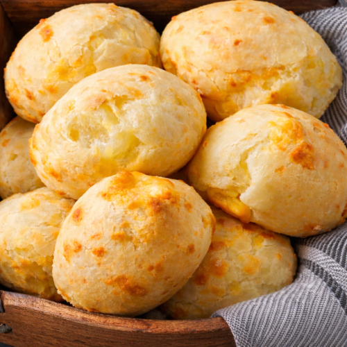 Freshly baked Brazilian cheese bread rolls arranged in a basket, showing golden cheese-speckled tops and a soft, airy texture.