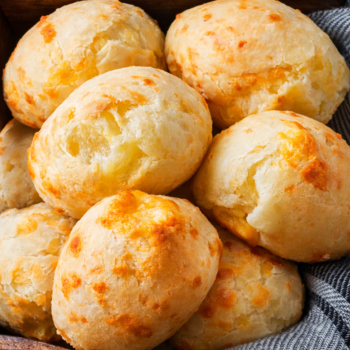 Freshly baked Brazilian cheese bread rolls arranged on parchment paper, showing golden cheese-speckled tops and a soft, airy texture.