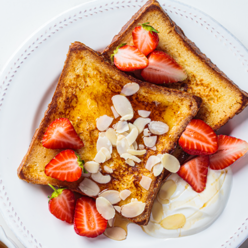A ceramic plate filled with French toast, fluffy whipped cream and berries.