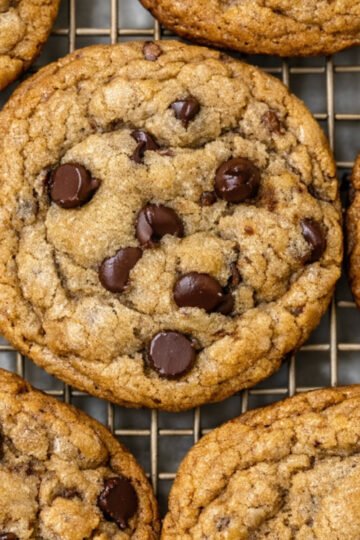 Thick, golden brown butter sourdough discard cookies laying on a plate, with melty chocolate puddles and crisp edges, showing their soft, chewy centers.