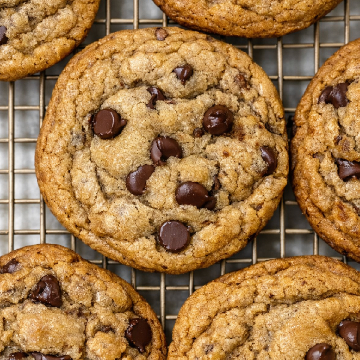 Thick, golden brown butter sourdough discard cookies laying on a plate, with melty chocolate puddles and crisp edges, showing their soft, chewy centers.