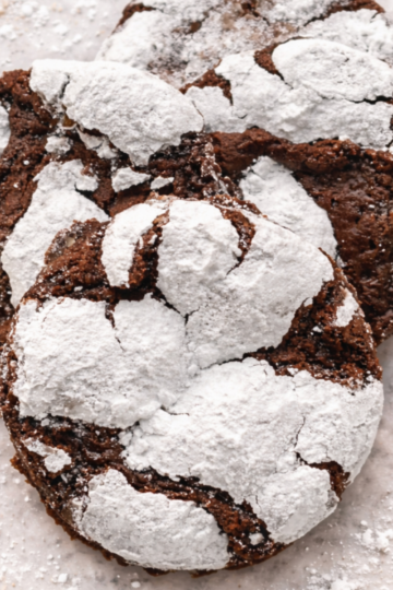 Gooey chocolate crinkle cookies with crackly powdered sugar tops and soft, chewy centers on a plate