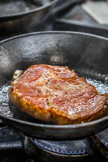 Close-up of golden-brown sear developing on meat in a hot pan, illustrating the Maillard reaction in cooking.