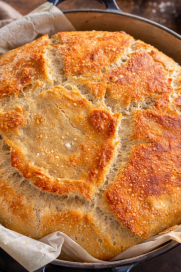 A golden, crusty sourdough loaf baked in a Dutch oven, resting on parchment paper with a light, airy crumb.