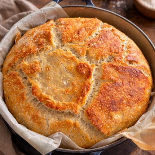 A golden, crusty sourdough loaf baked in a Dutch oven, resting on parchment paper with a light, airy crumb.