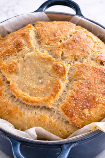 A golden, crusty sourdough loaf baked in a Dutch oven, resting on parchment paper with a light, airy crumb.