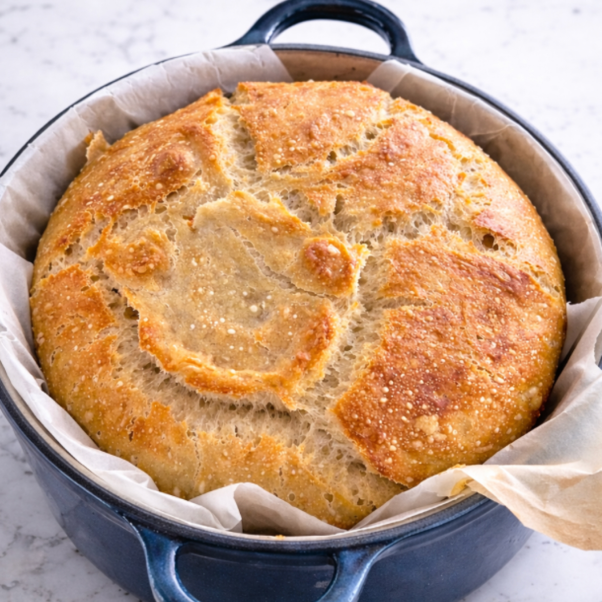 A golden, crusty sourdough loaf baked in a Dutch oven, resting on parchment paper with a light, airy crumb.