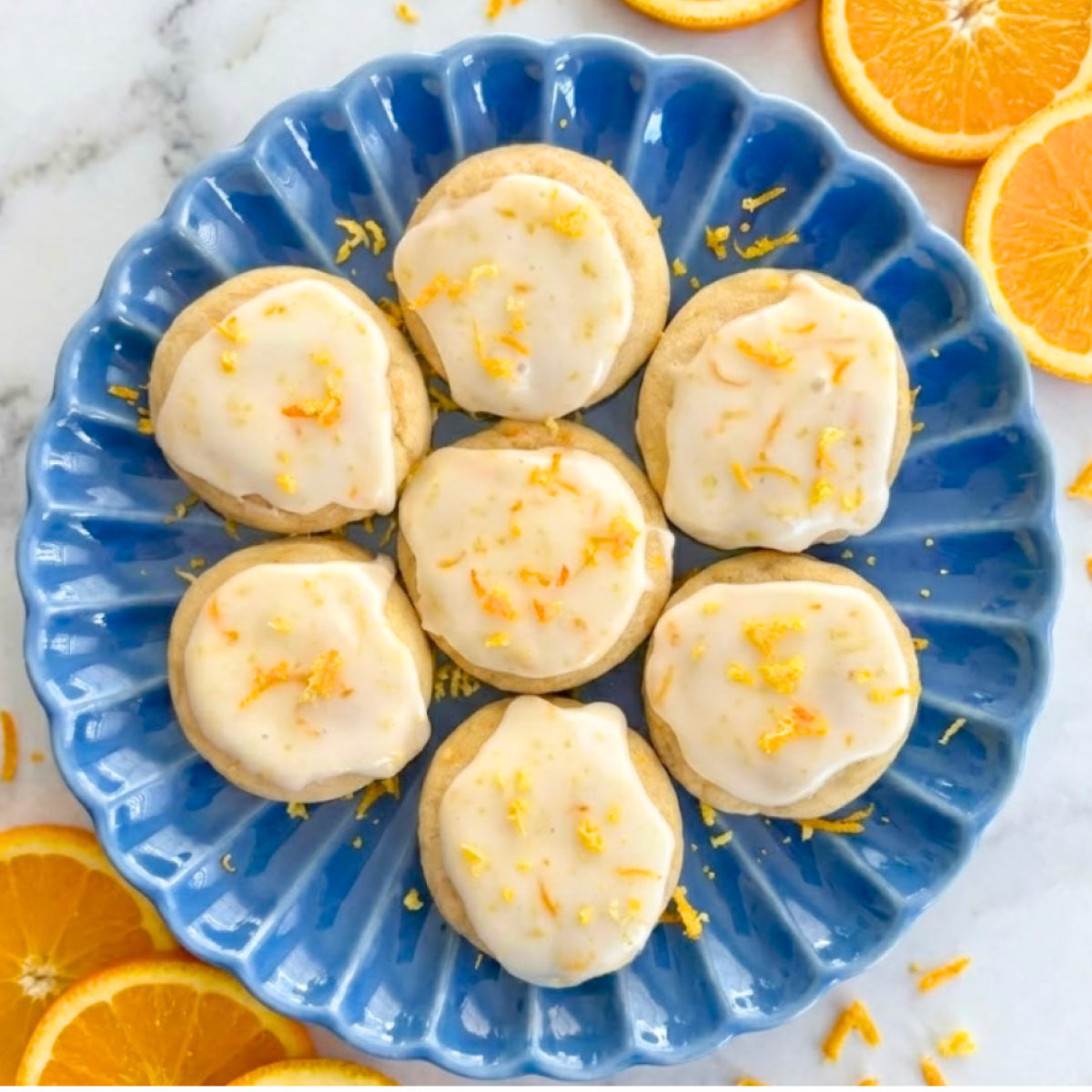 Frosted citrus cookies topped with a crackly orange glaze and fresh citrus zest on a serving dish.