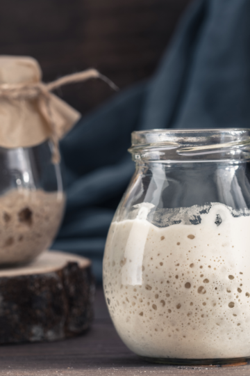 A bubbly sourdough starter in a clear jar showing fermentation activity, used to illustrate baking science, feeding ratios, and troubleshooting starter issues.