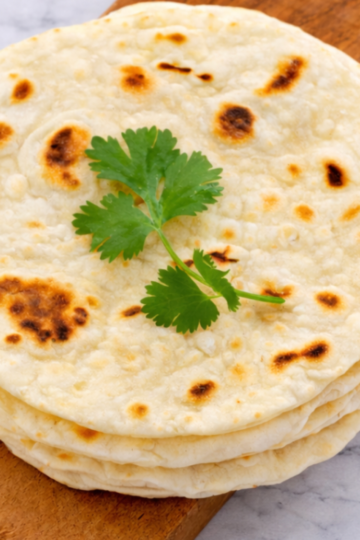 Soft homemade naan bread cooked in a skillet and ready to be brushed with butter.