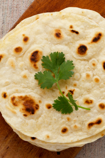 Soft homemade naan bread cooked in a skillet and ready to be brushed with butter.