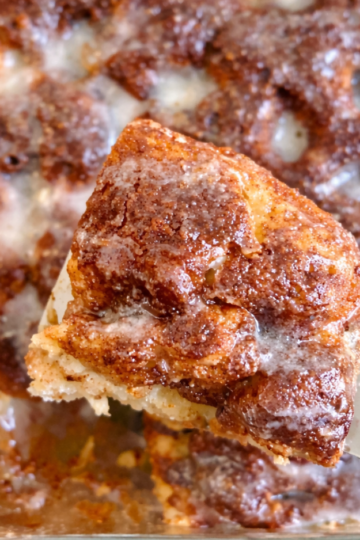 Golden sourdough discard cinnamon roll focaccia bread baked in a 9x13 pan with cinnamon sugar swirls and a glossy vanilla glaze drizzled on top.