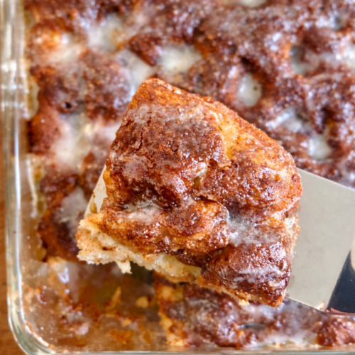 Golden sourdough discard cinnamon roll focaccia bread baked in a 9x13 pan with cinnamon sugar swirls and a glossy vanilla glaze drizzled on top.