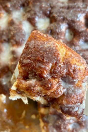 Golden sourdough discard cinnamon roll focaccia bread baked in a 9x13 pan with cinnamon sugar swirls and a glossy vanilla glaze drizzled on top.