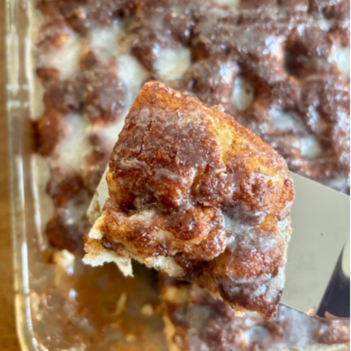 Golden sourdough discard cinnamon roll focaccia bread baked in a 9x13 pan with cinnamon sugar swirls and a glossy vanilla glaze drizzled on top.