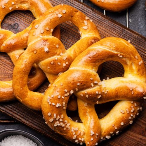 Freshly baked golden-brown sourdough pretzels with coarse sea salt on a cutting board.