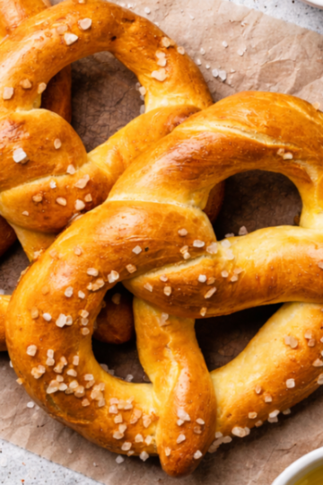Freshly baked golden-brown sourdough pretzels with coarse sea salt on a counter.