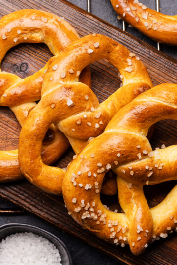 Freshly baked golden-brown sourdough pretzels with coarse sea salt on a cutting board.