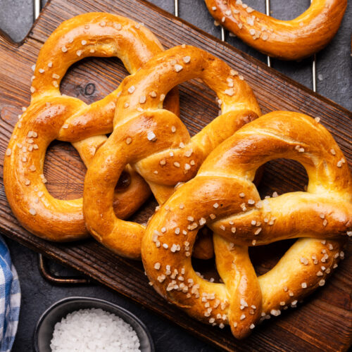Freshly baked golden-brown sourdough pretzels with coarse sea salt on a cutting board.