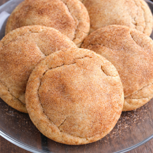 Brown butter snickerdoodle cookies stacked on a glass plate with cinnamon sugar coating and golden edges.