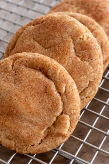 Brown butter snickerdoodle cookies stacked on a cooling rack with cinnamon sugar coating and golden edges.