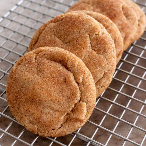 Brown butter snickerdoodle cookies stacked on a cooling rack with cinnamon sugar coating and golden edges.