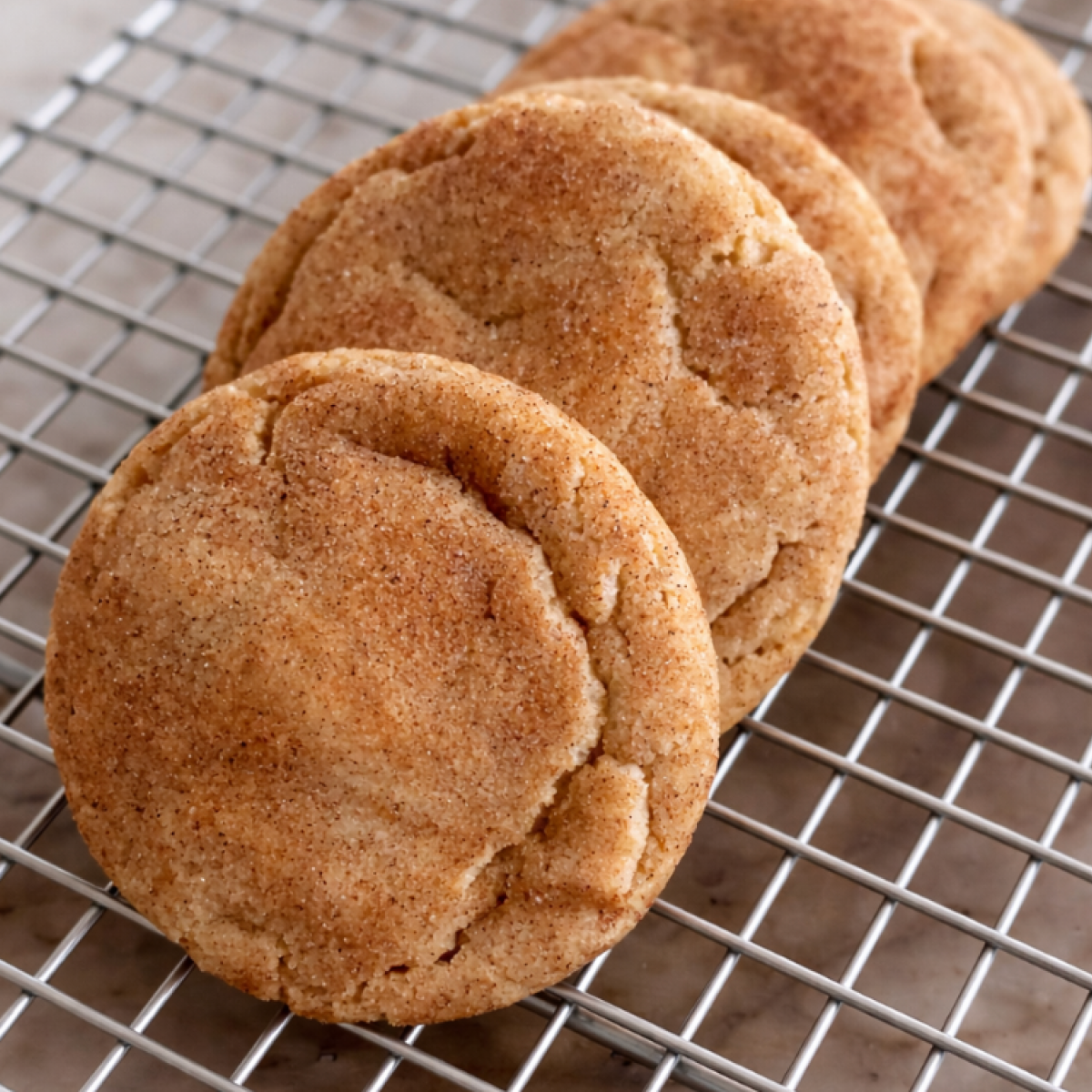 Brown butter snickerdoodle cookies stacked on a cooling rack with cinnamon sugar coating and golden edges.