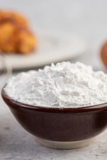 A small brown bowl filled to the brim with baking powder sitting on a nice white countertop.