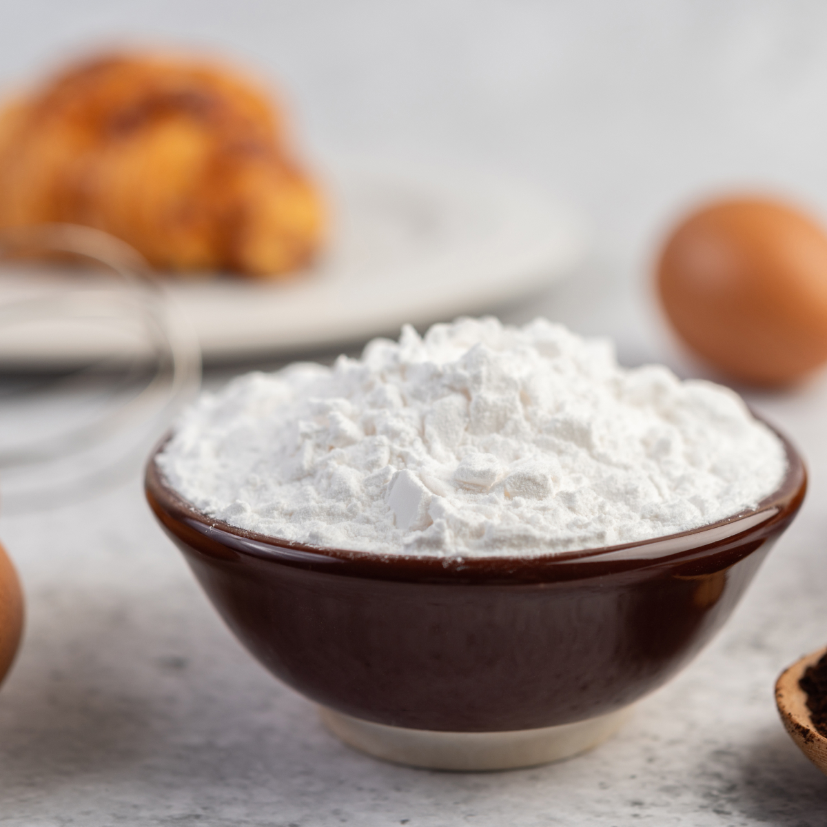 A small brown bowl filled to the brim with baking powder sitting on a nice white countertop.