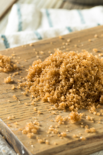 A wooden cutting board with golden brown sugar in 2 piles on top.