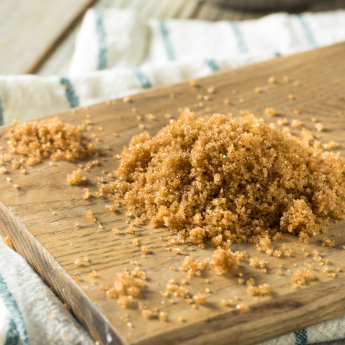 A wooden cutting board with golden brown sugar in 2 piles on top.