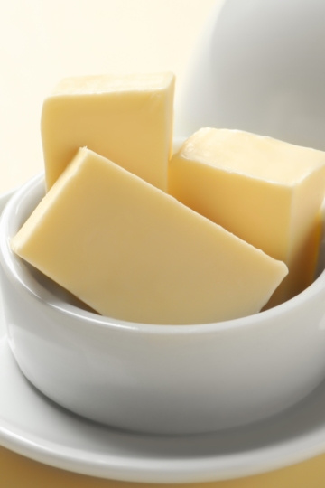 A nice ceramic butter dish filled with sticks of yellow butter sitting on a nice countertop.