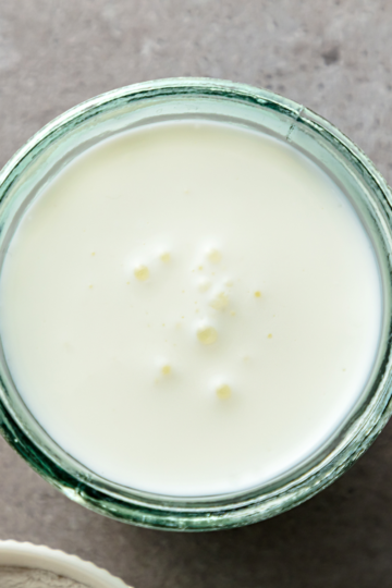 A nice glass container filled with rich buttermilk sitting on a countertop.