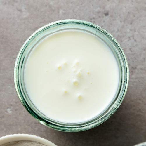 A nice glass container filled with rich buttermilk sitting on a countertop.