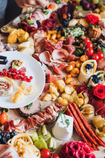 A long party table filled with colorful cheeses, meats, fruits and berries creating a lovely charcuterie board.