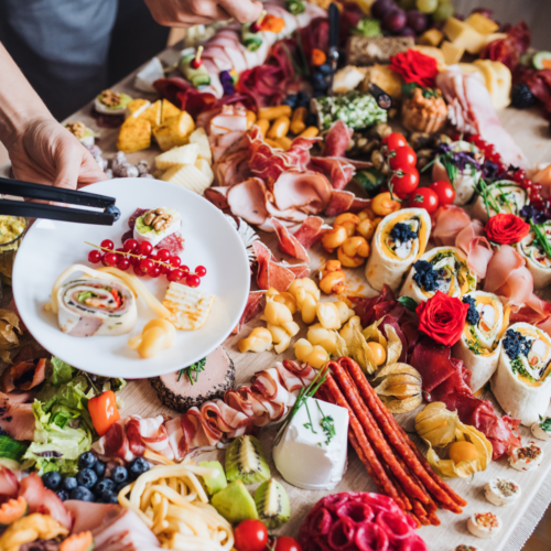 A long party table filled with colorful cheeses, meats, fruits and berries creating a lovely charcuterie board.