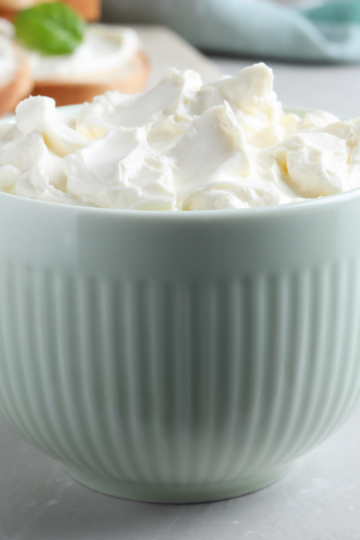 A ceramic blue bowl filled with fluffy cream cheese sitting on a nice clean countertop.