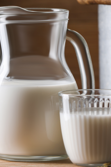 A nice glass pitcher filled with heavy cream sitting on a wooden table along side a glass cup of heavy cream.