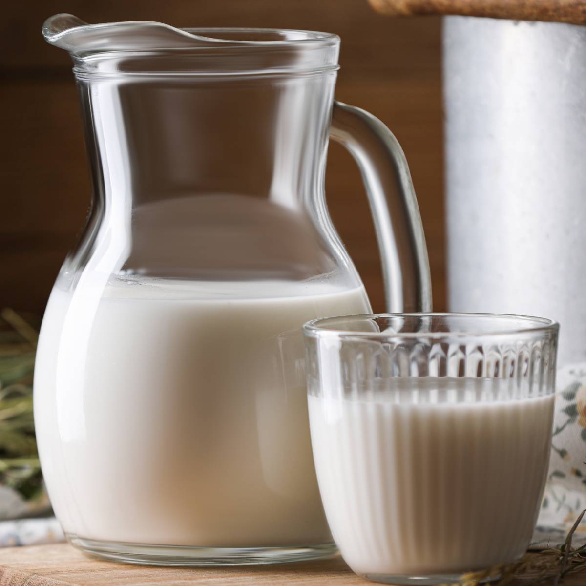 A nice glass pitcher filled with heavy cream sitting on a wooden table along side a glass cup of heavy cream.