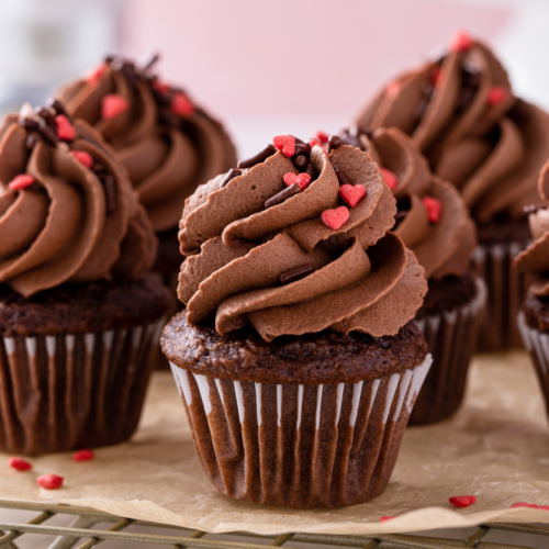 A beautiful chocolate cupcake frosted with chocolate frosting and topped with heart shaped sprinkles.
