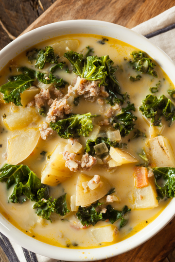 A warm bowl of Zupa Toscana soup on a nice rustic wooden table.