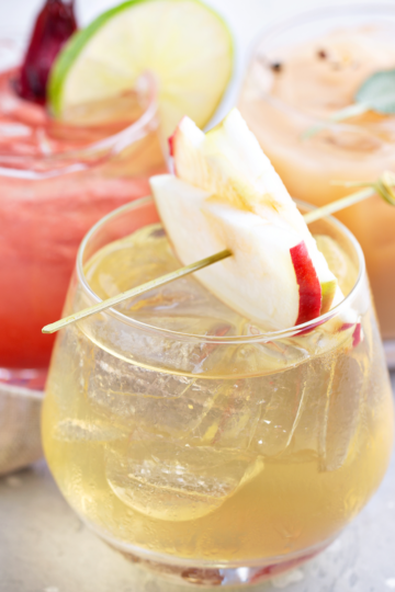 Nice glasses filled with colorful drinks and ice. Topped with fruit and sitting on a clean countertop.