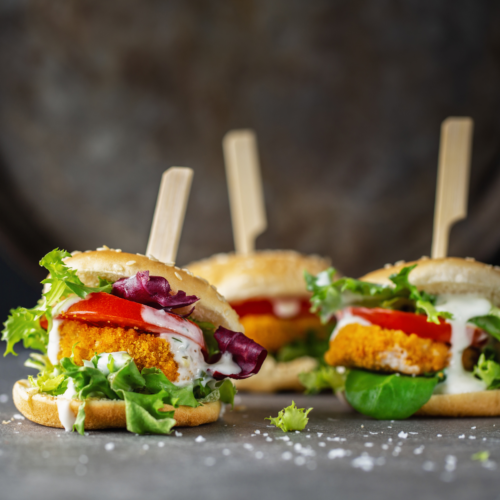 Counter of mini burger sliders with lettuce and tomato arranged ready for a party food planning guide.