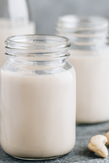 A couple of nice glass jars filled with white nut milk sitting on a nice counter.